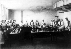 Black and white photo of a large group of young girls using electric stove tops. 