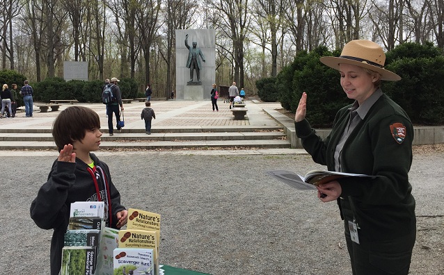 Ranger swearing in a Junior Ranger with a statue of Theodore Roosevelt in the distance