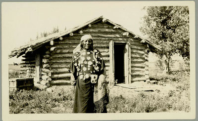 A man standing in front of a small wood cabin