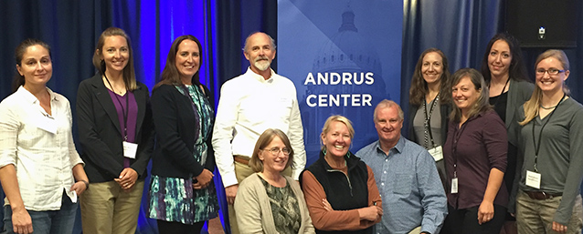 Men and women in front of blue curtain and Andrus Center banner.