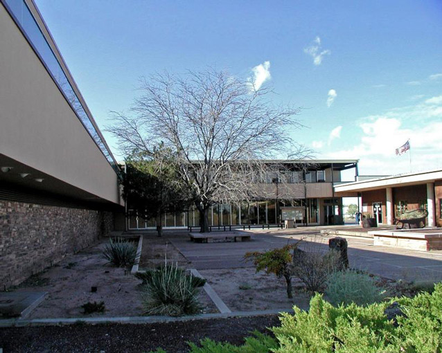 Rectangular buildings surround an open courtyard, containing some benches, trees, and plantings.