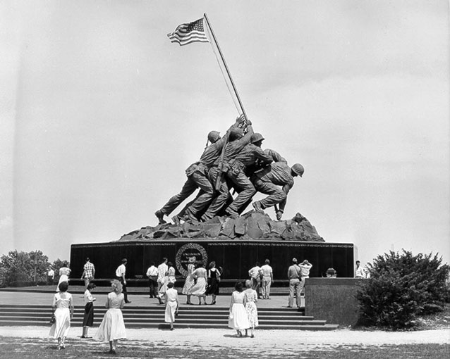 Women and men stand at the base of a monument, depicting U.S. armed forces raising a flag. 