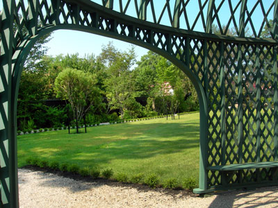 A green lawn extends beyond the framework of an arching green pergola.