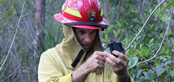 A man in fire-resistant gear and hardhat looks at a compass.