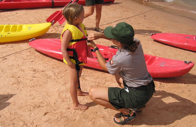 NPS Ranger helping a young child put on a properly fitted U.S. Coast Guard approved life jacket