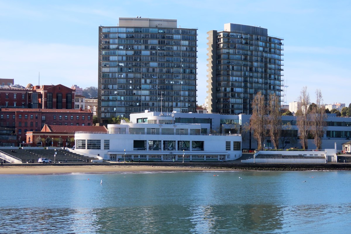 A view of a large white building standing next to a beach and the calm water of a cove