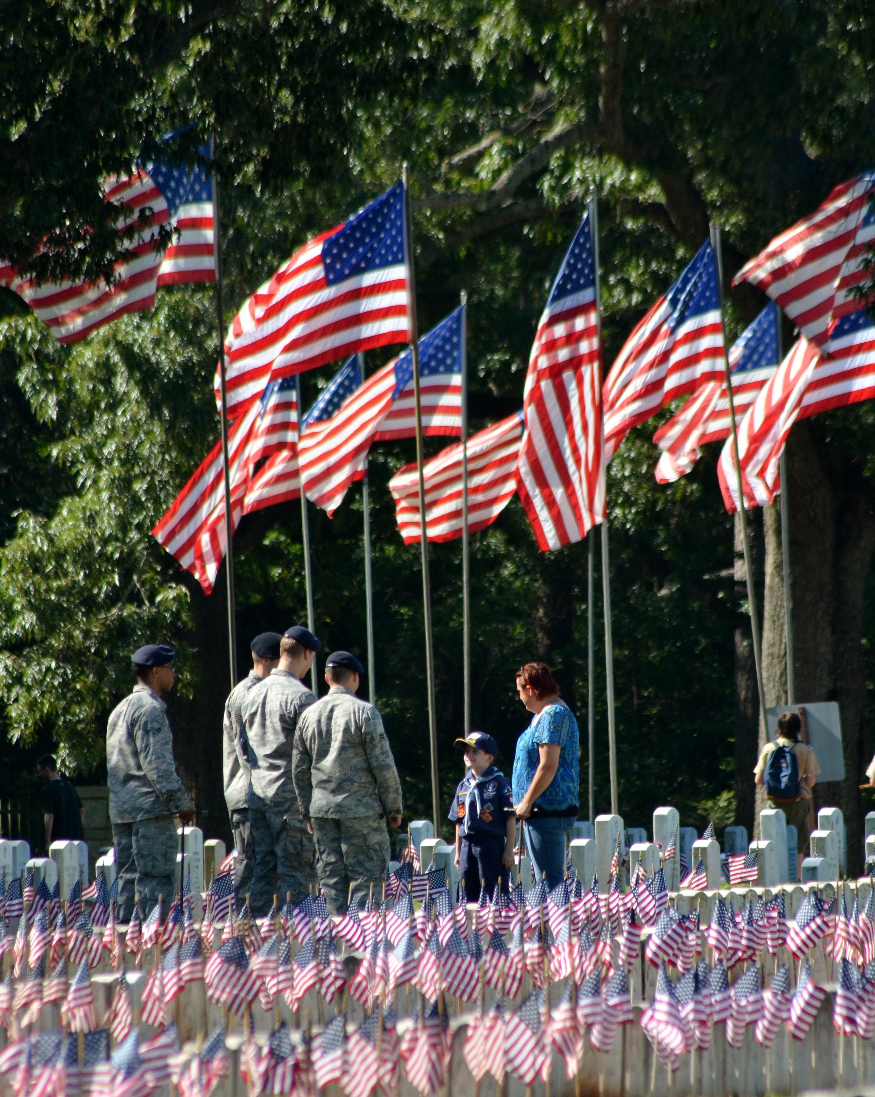 Soldiers talk to a Boy Scout in a cemetery with small US flags decorating the headstones