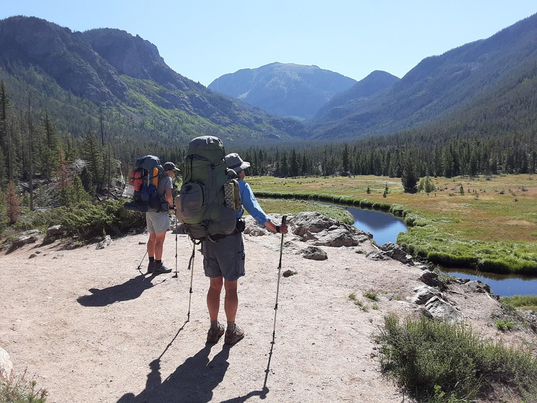 Two wilderness campers are carrying big backpacks on the East Inlet Trail