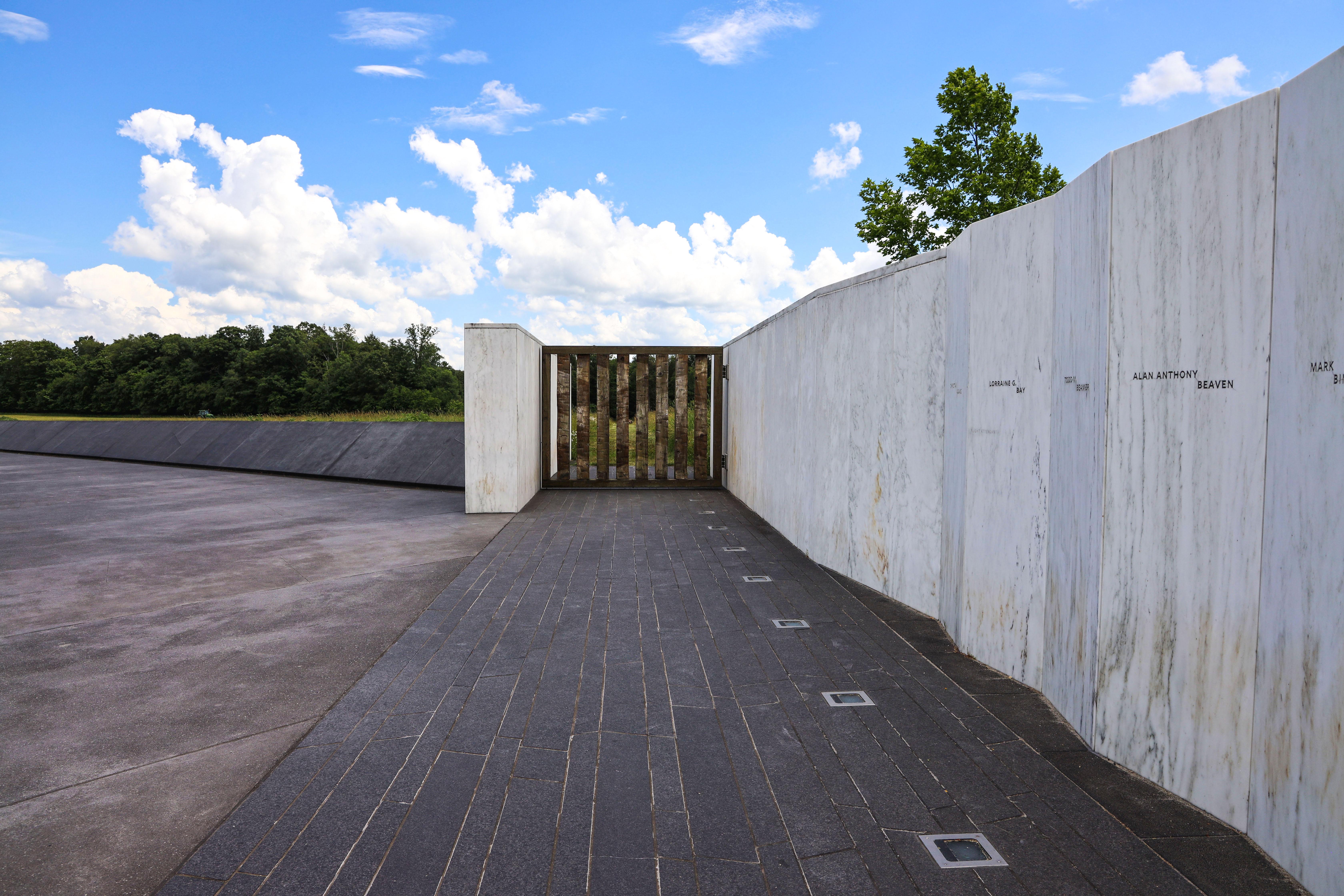 A white marble wall with names engraved on the the walls and the Ceremonial Gate. Blue sky above.