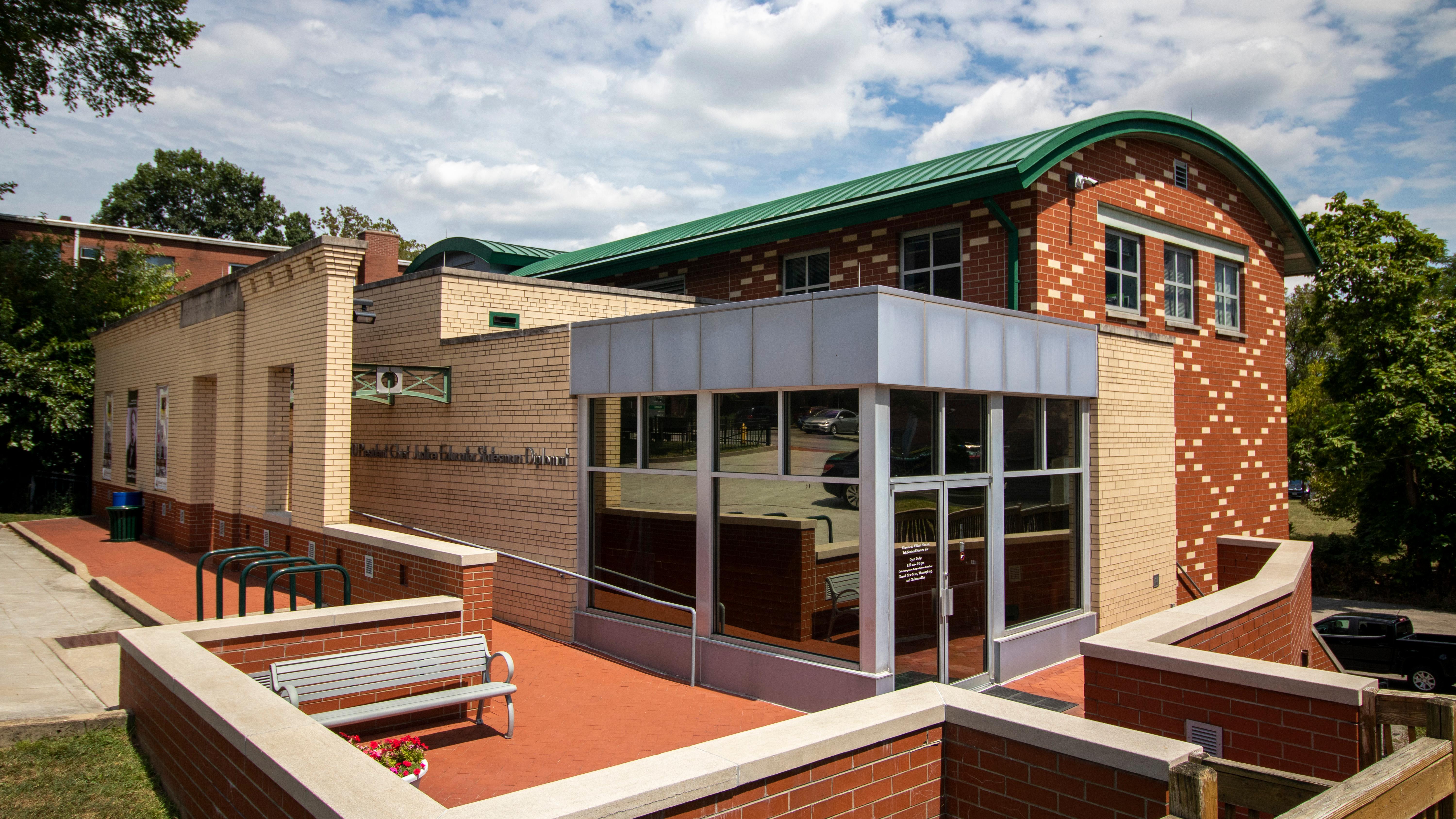 A tan and brick sided building with a corner entrance featuring tall glass windows and doors.