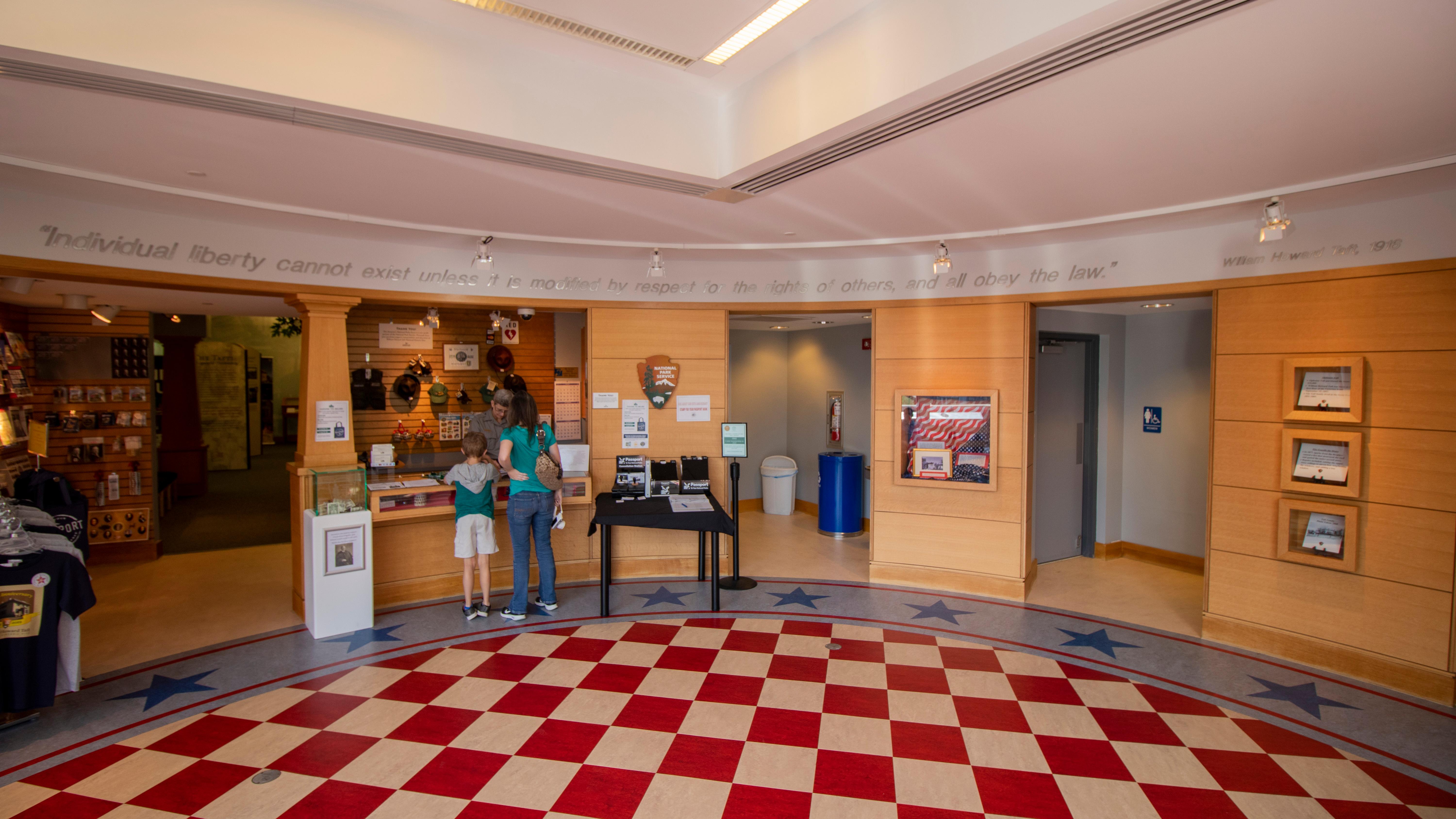 A lobby area with red and white square tiles and two people standing at a counter with a ranger.