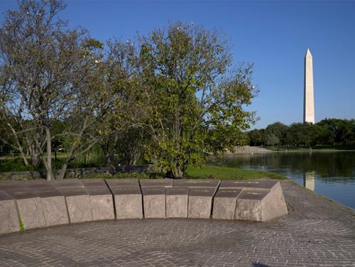 A low stone semicircle adjacent to a lake with the Washington Monument in the background.