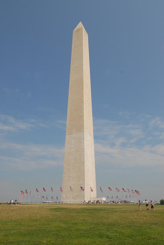 The Washington Monument, a white marble obelisk, towers above a ring of US Flags.