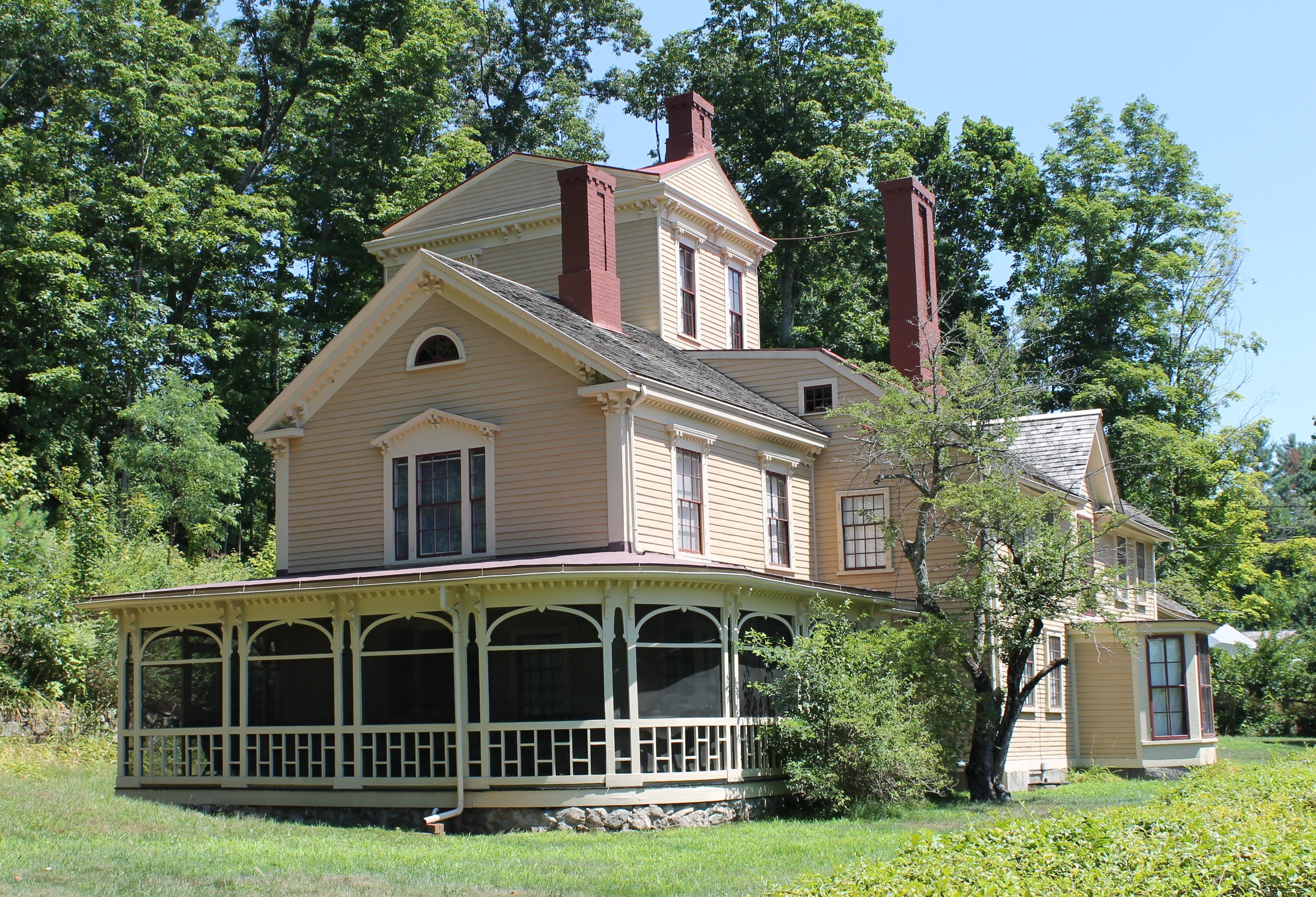 A large mansion house made of wood with wrap around porch and tower room. Surrounded by large trees