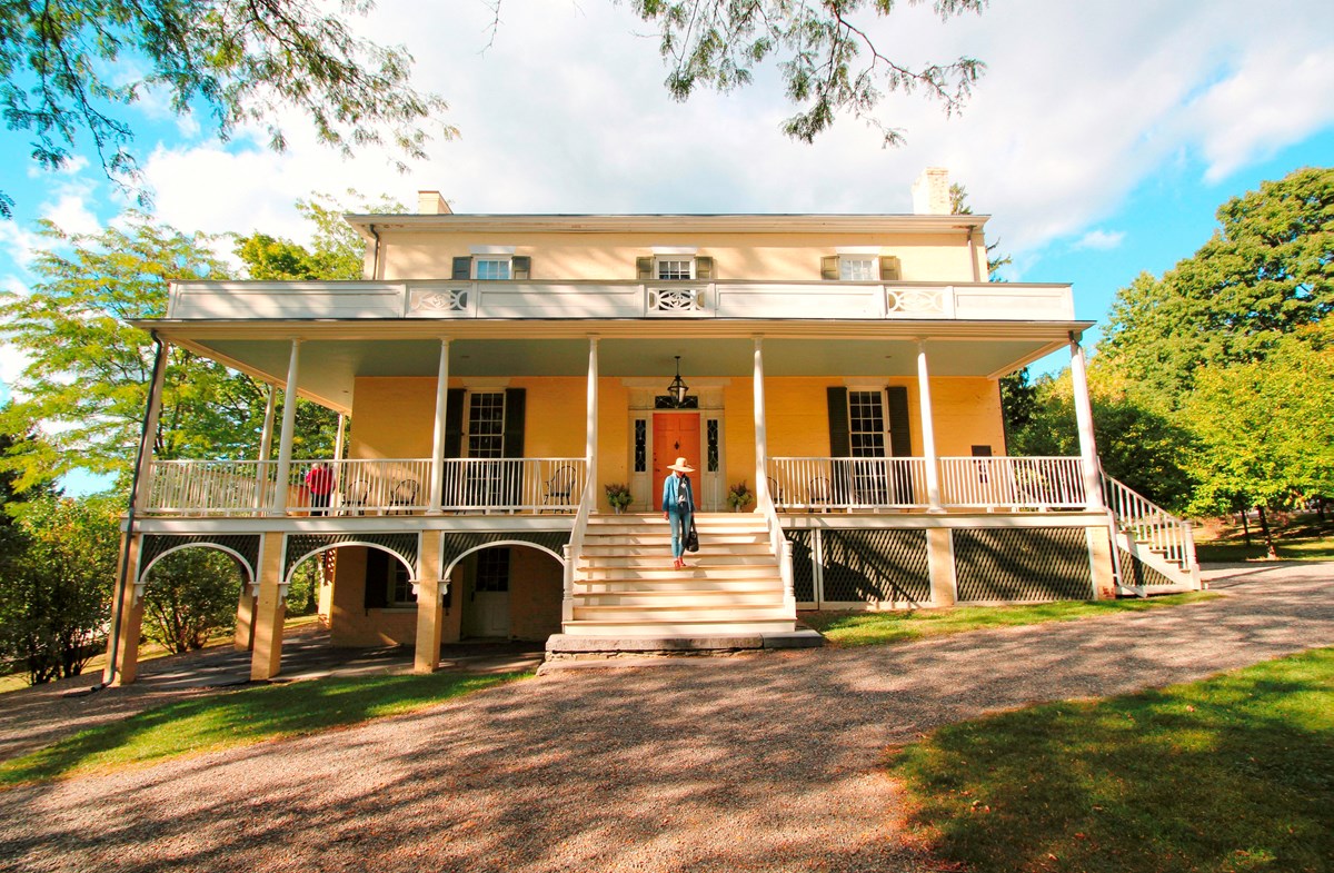 A three story house with large porch across the front and flight of steps leading to the ground. 