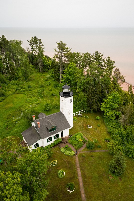 Photograph of historic lighthouse from above with Lake Superior in the background.