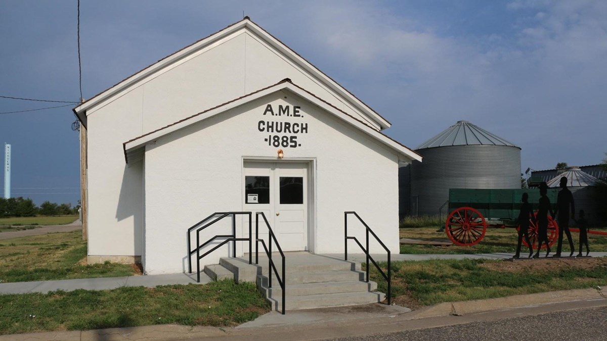 A stucco building painted white with a green wagon out front.