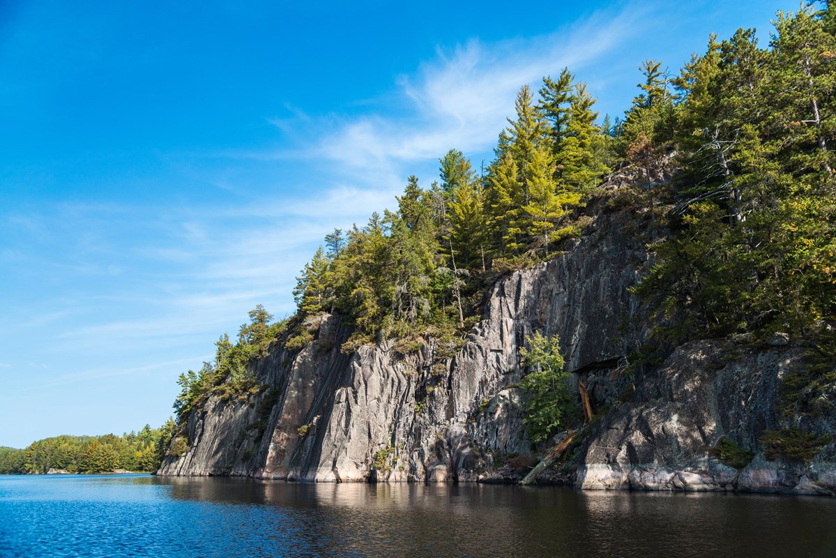 Photograph of granite cliffs topped with trees alongside a blue lake.