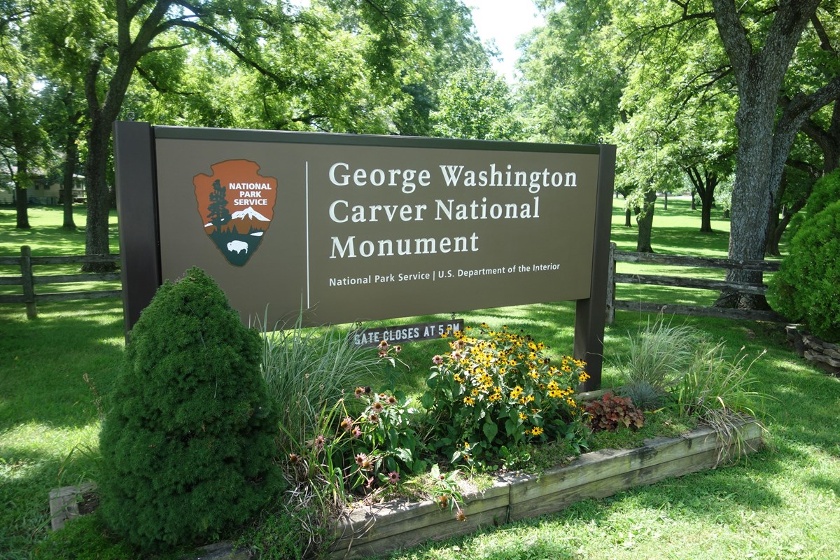 An entrance sign to George Washington Carver National Monument with wildflower and plants. 