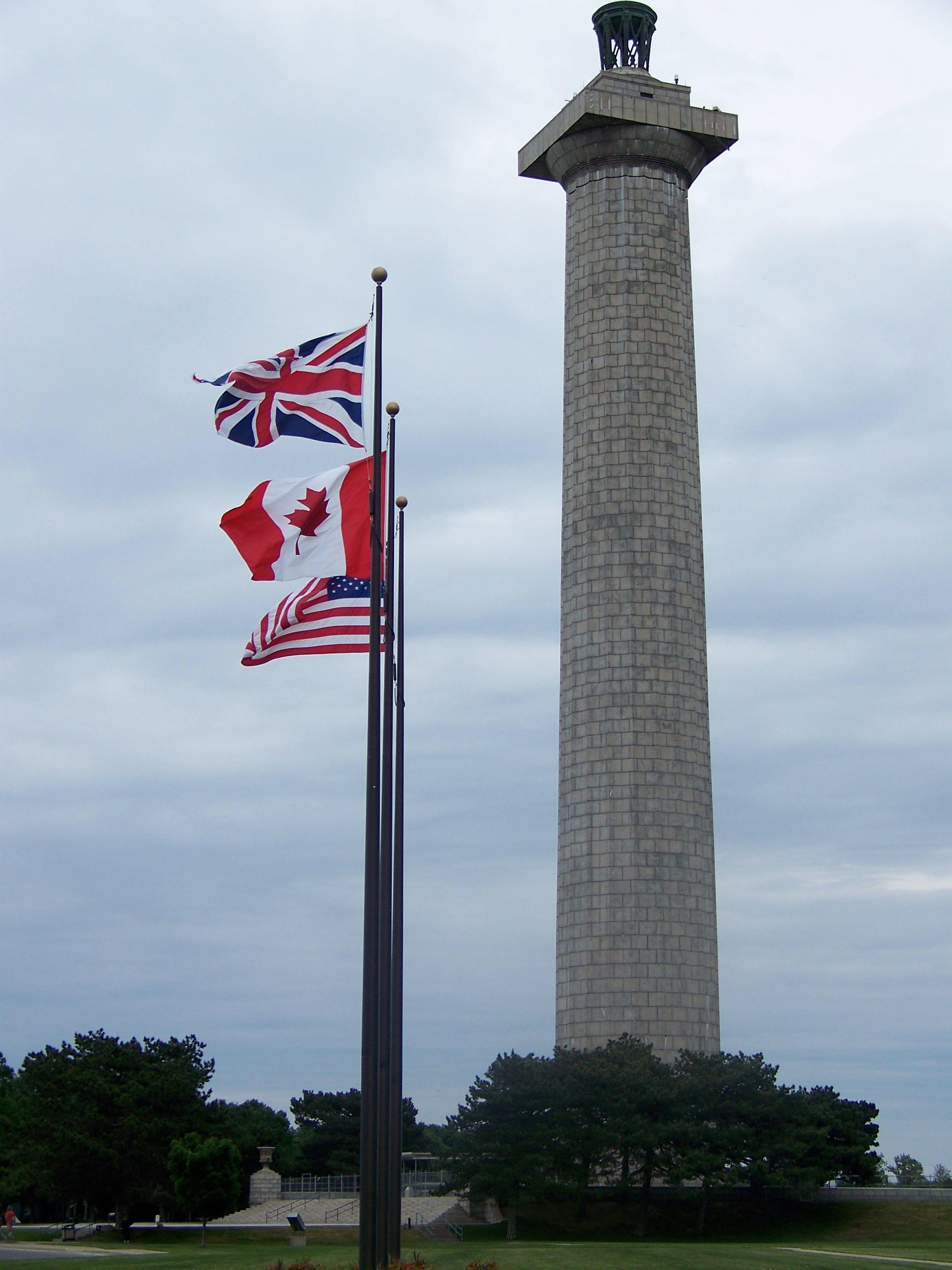 The Memorial Column with the United Kingdom, Canadian, and US Flags flying from poles on the lawn.