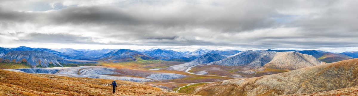 Hiker on the tundra. Snow covered mountains and a river in the dramatic background.