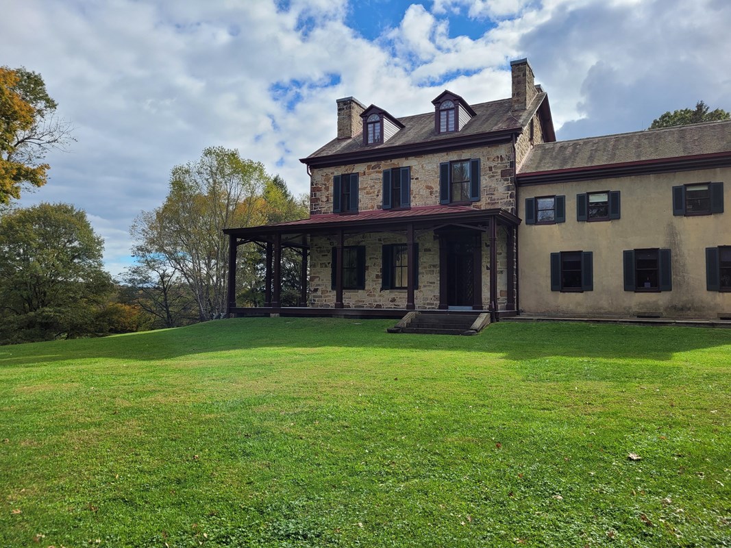 front view of historical Stone House and Visitor Center with green grass lawn with trees and clouds