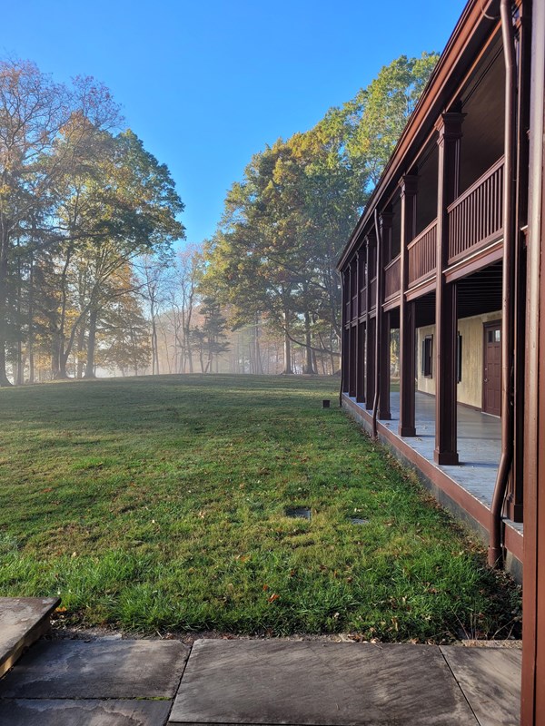Foggy forest in background with historic house on right with a double storied porch