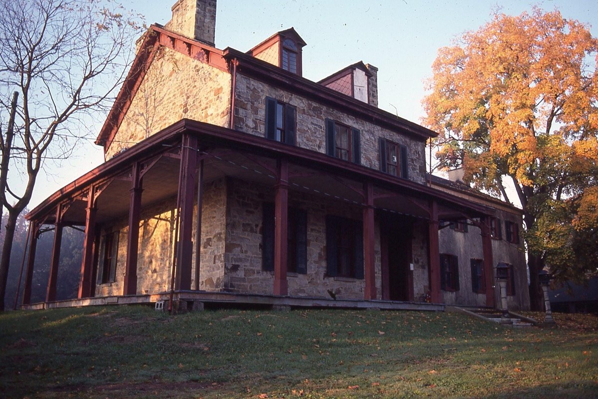 sun rising over a historical two and a half story stone house with trees in fall colors