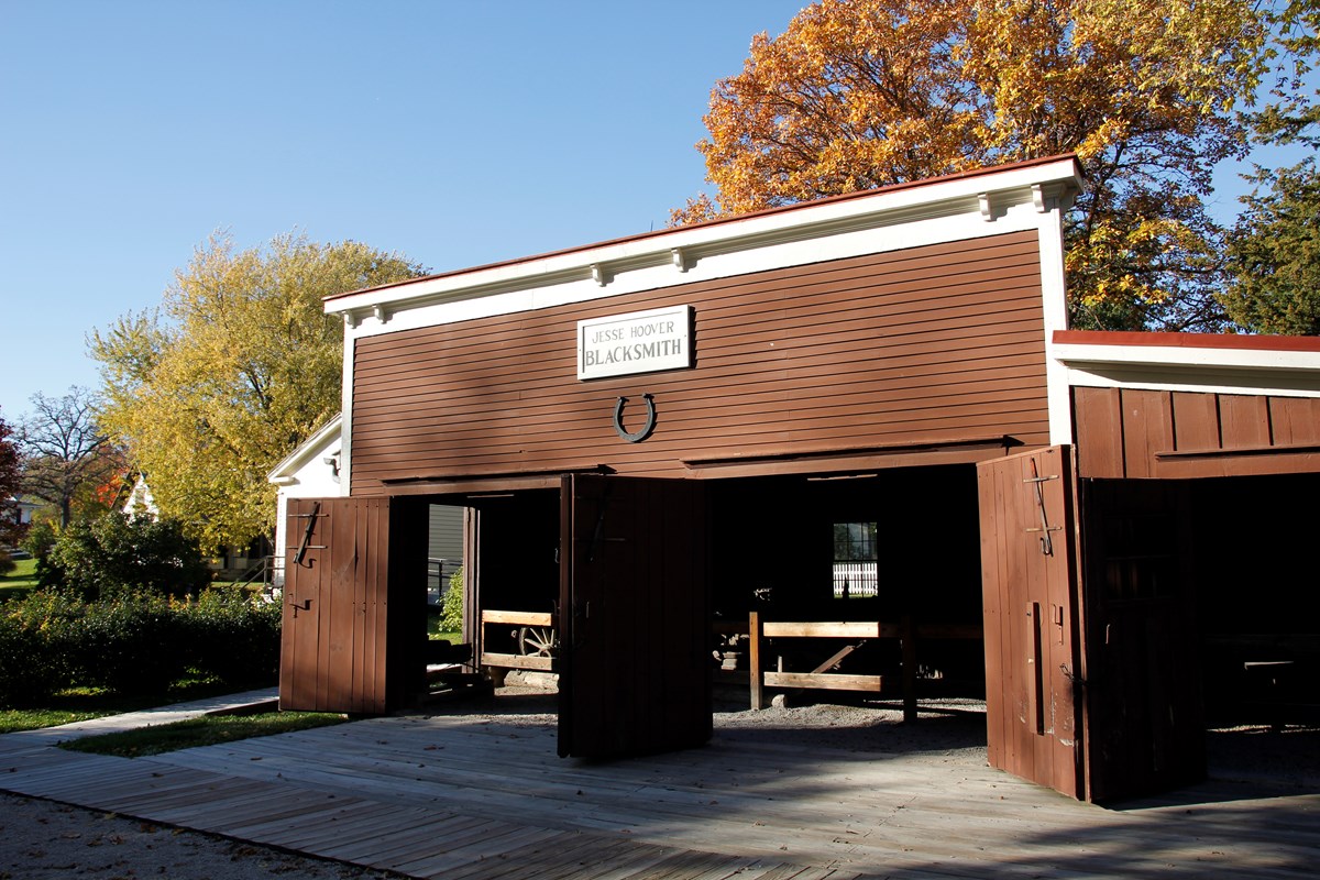 A low brown barn-like building with three large doorways has a large horseshoe on its facade. 