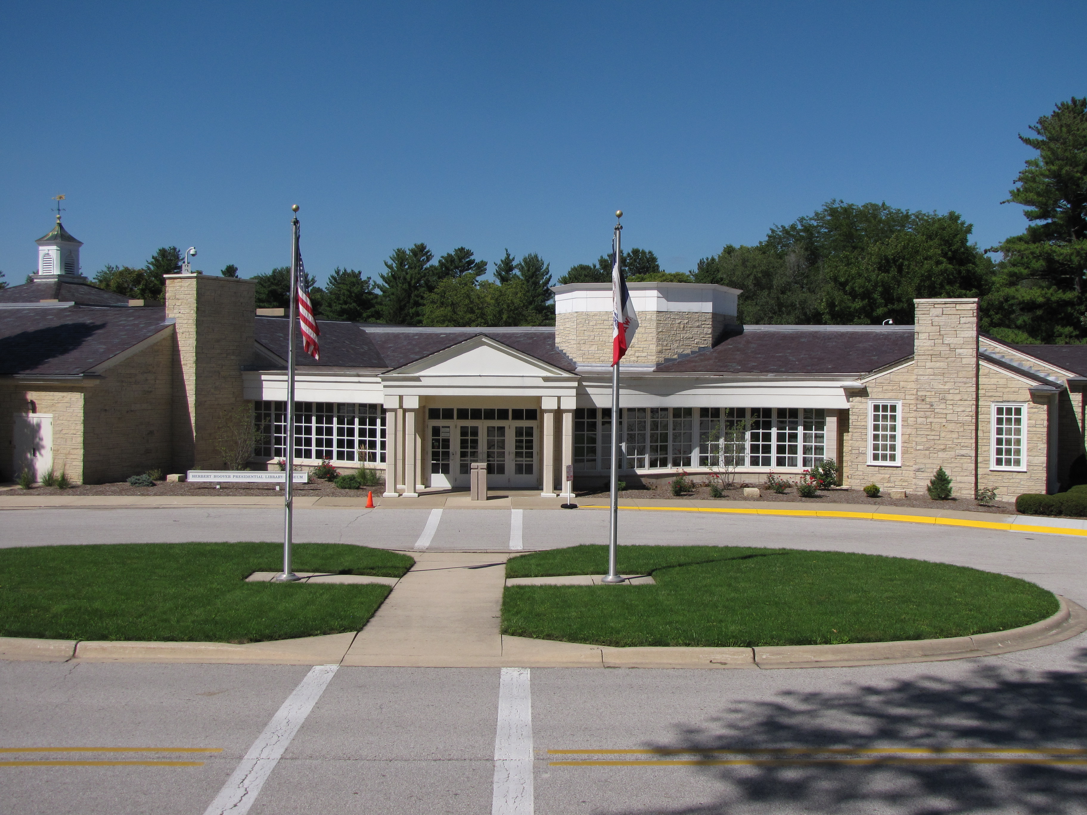 A sprawling one story public building of rough-faced yellowish stone has a white portico entrance.