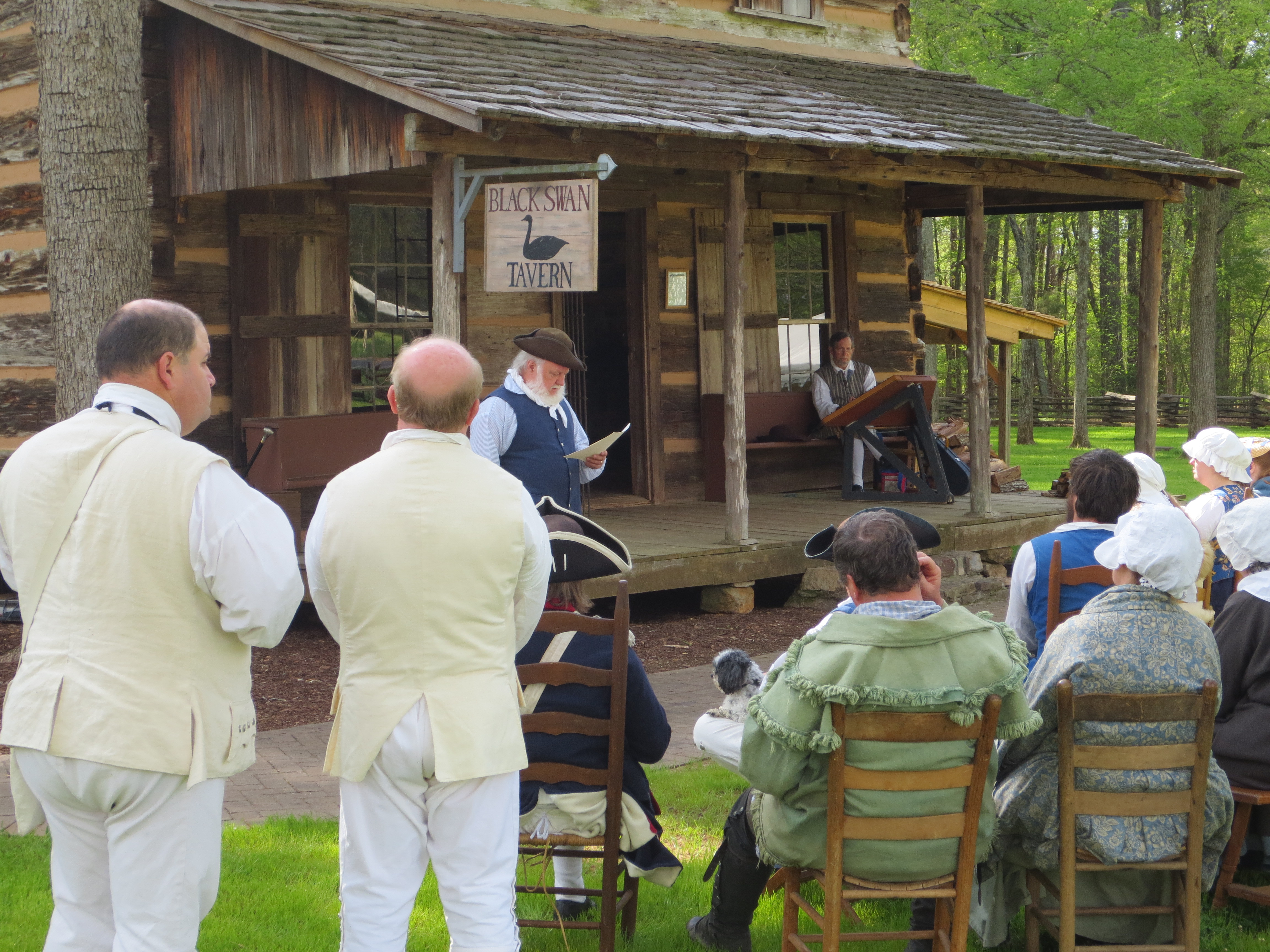 Reenactors listen as another reenactor presents and 18th century church service.