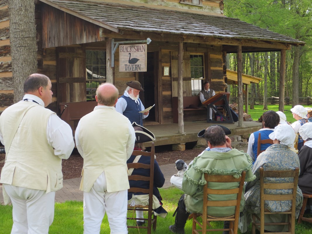 Reenactors listen as another reenactor presents and 18th century church service.