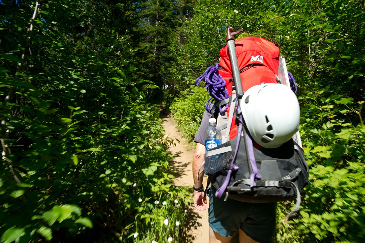 Person with backpacking and climbing gear hikes on a trail. 