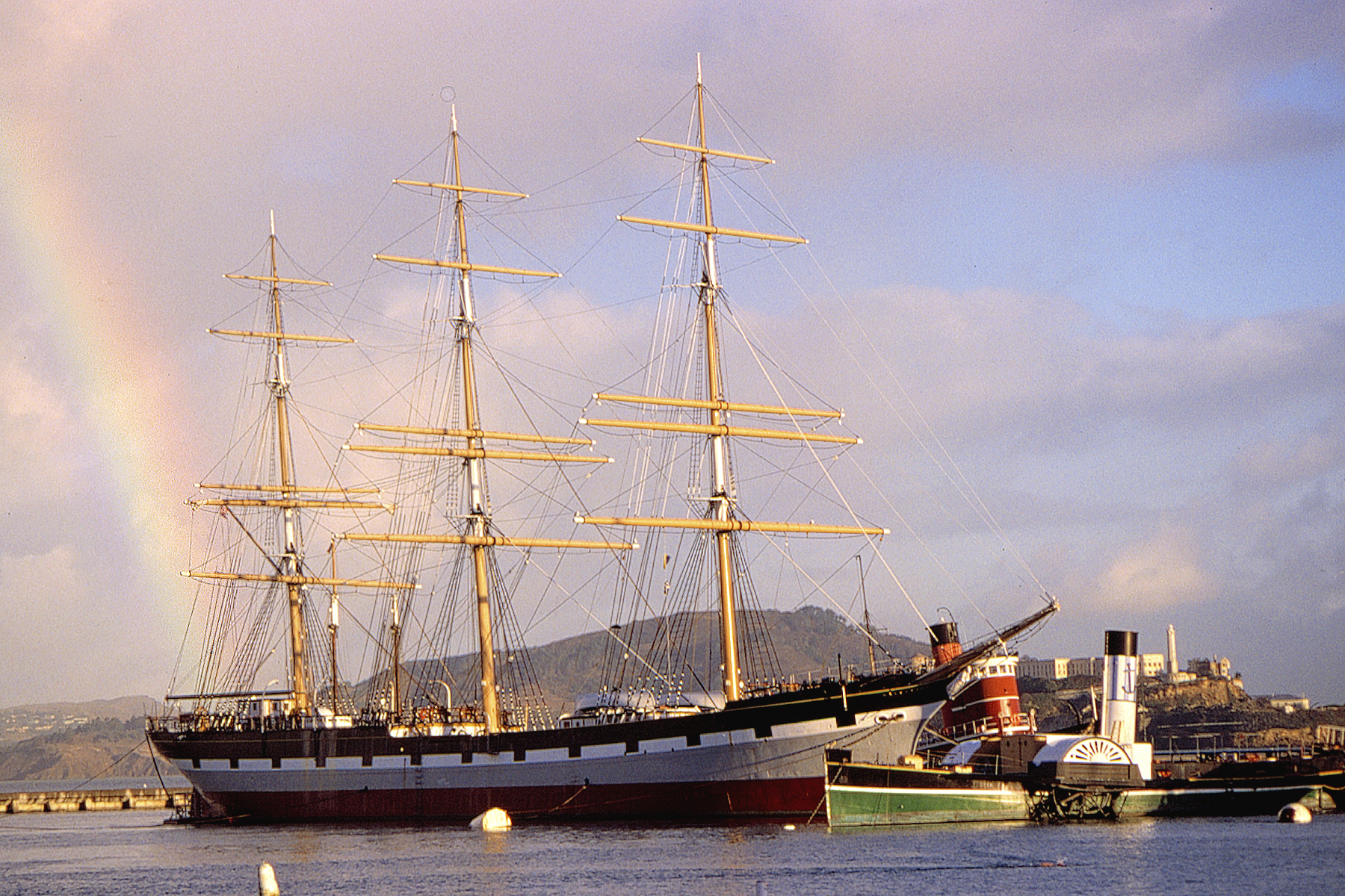 A group of vessels moored at a pier with a rainbow.