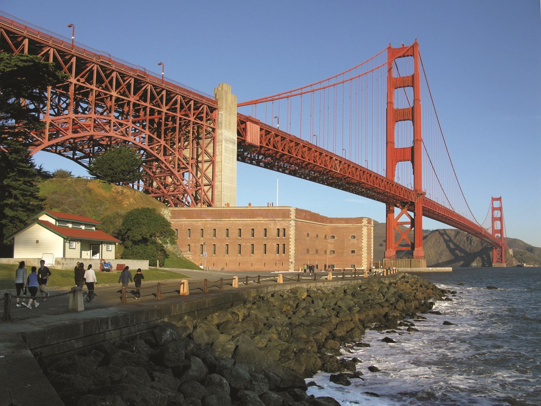 Fort Point with visitors approaching on road in front and Golden Gate Bridge above.