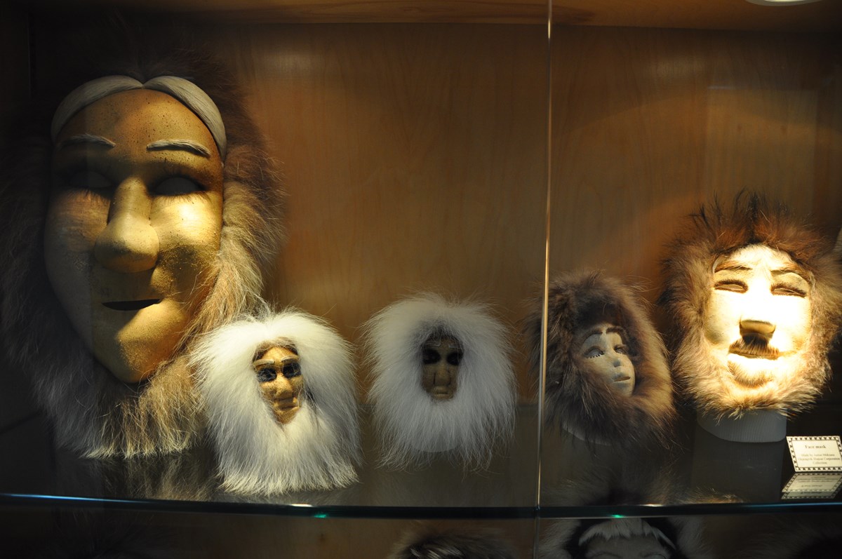 Five masks with fur trim in a display case.