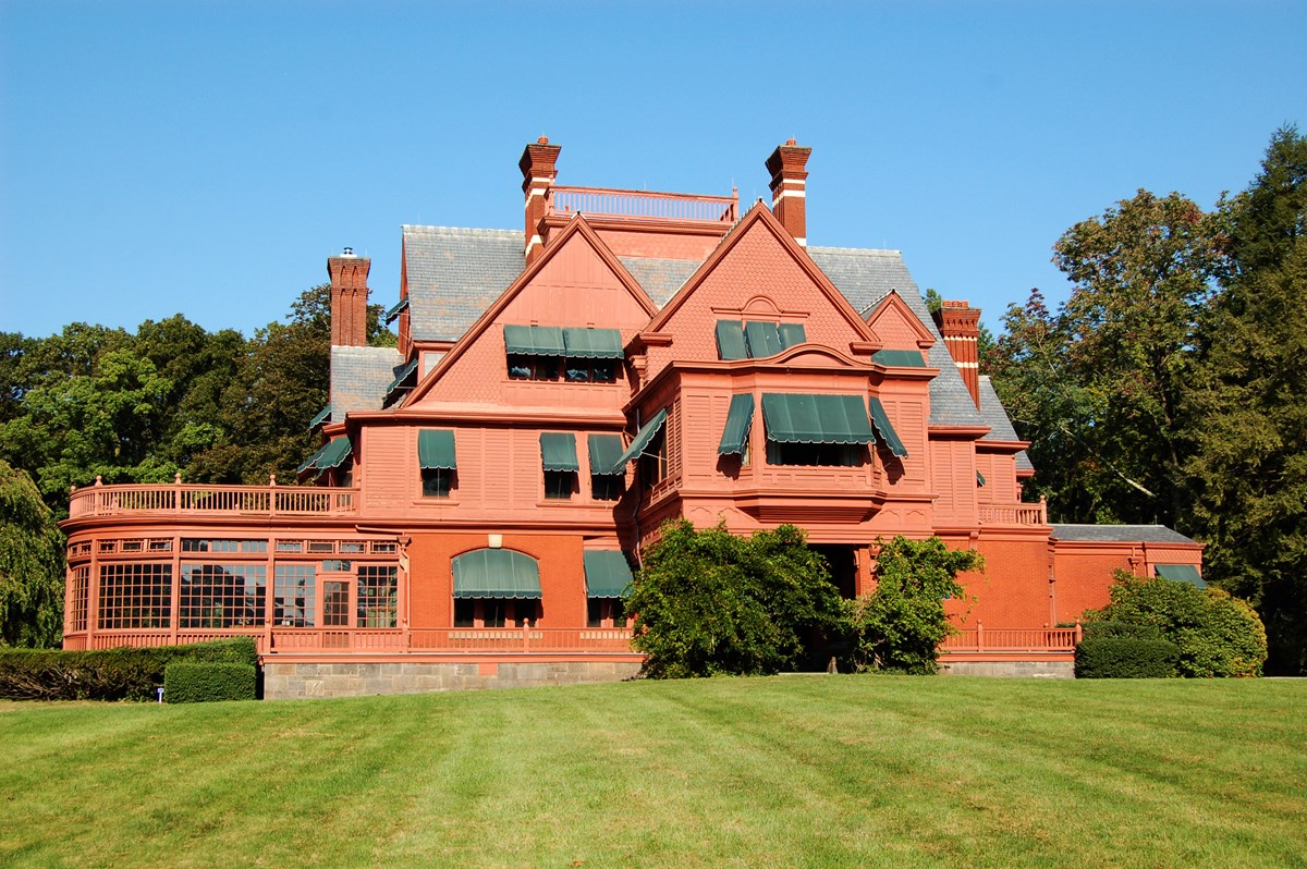 Large salmon colored Victorian mansion with green lawn and blue sky