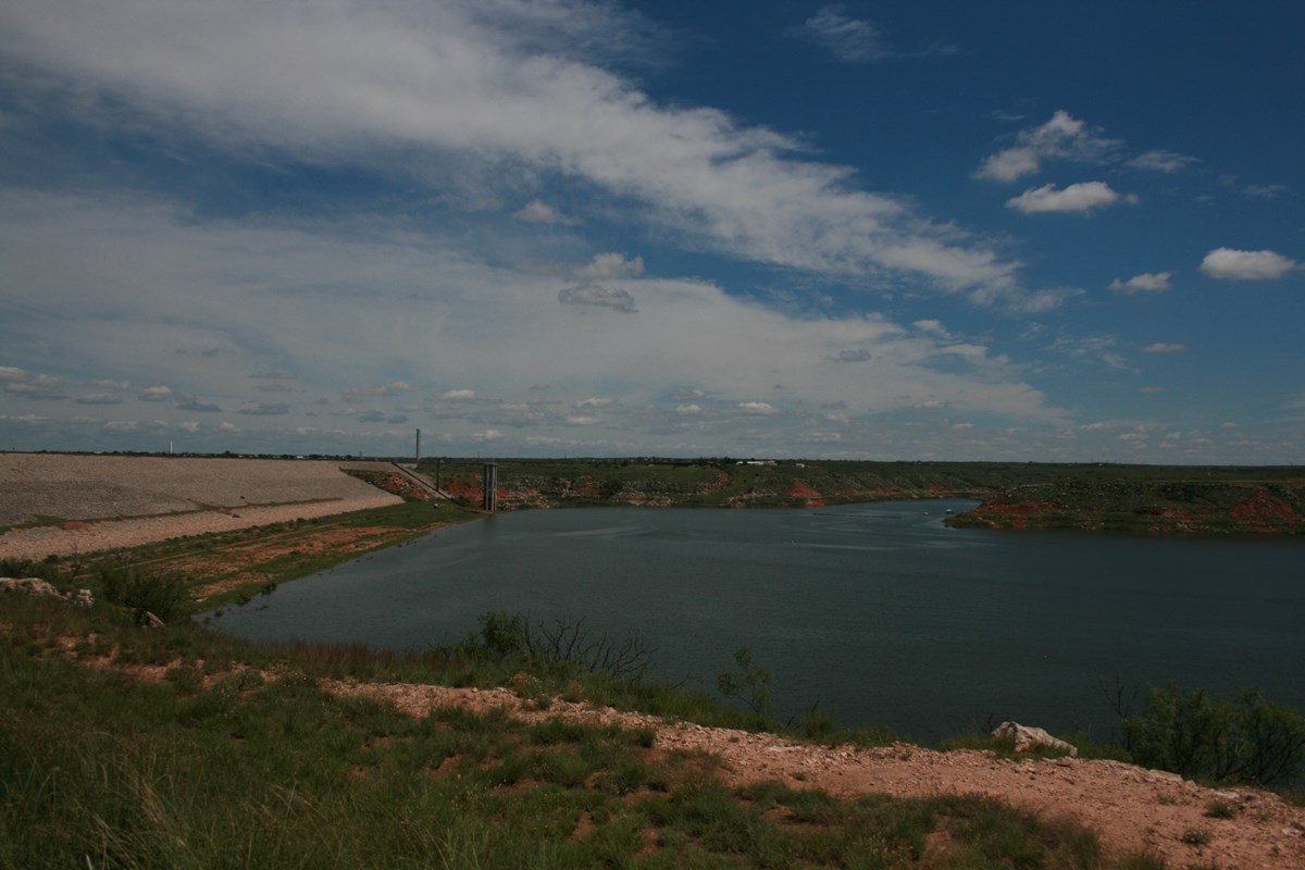 Sanford Dam and Lake Meredith.  The lake is deep blue with white clouds above in the sky. 
