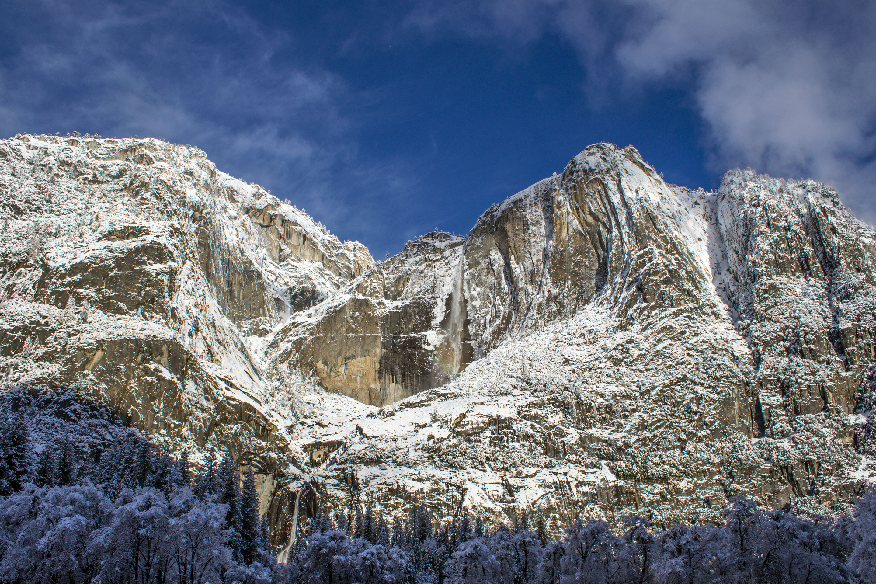 Two tall waterfalls flowing down snow covered granite walls.