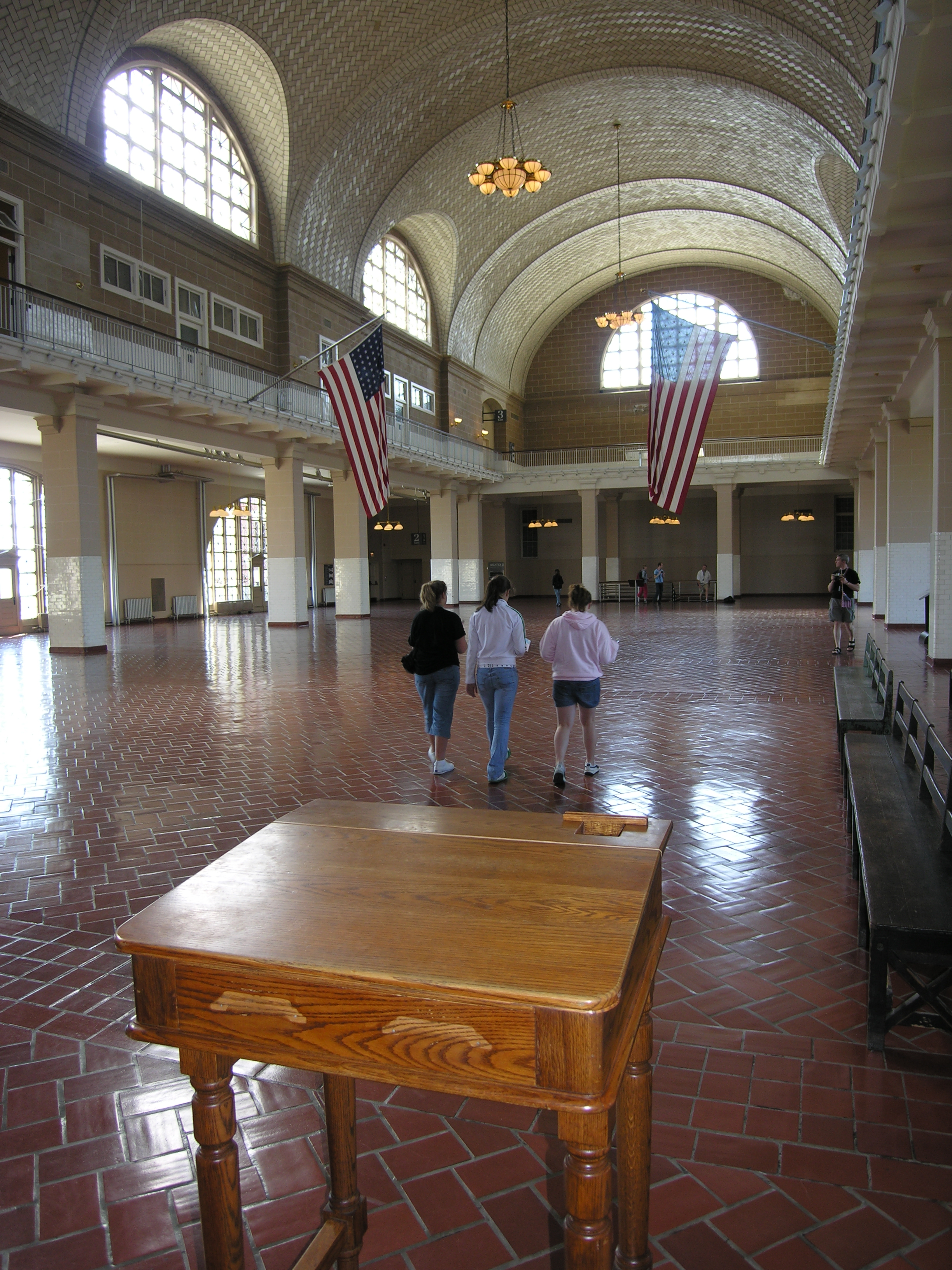 Honey oak colored tall desk on tiled floor in Great Hall with arched windows and vaulted ceiling.