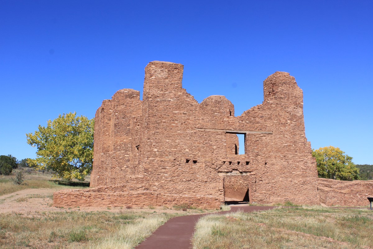 Stone walls of a roofless building rise into a bright blue sky. 