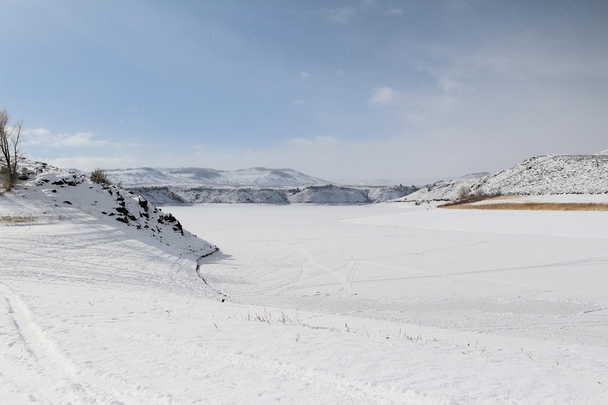 Frozen over body of water with snow covering it. Mesas are on the edge.
