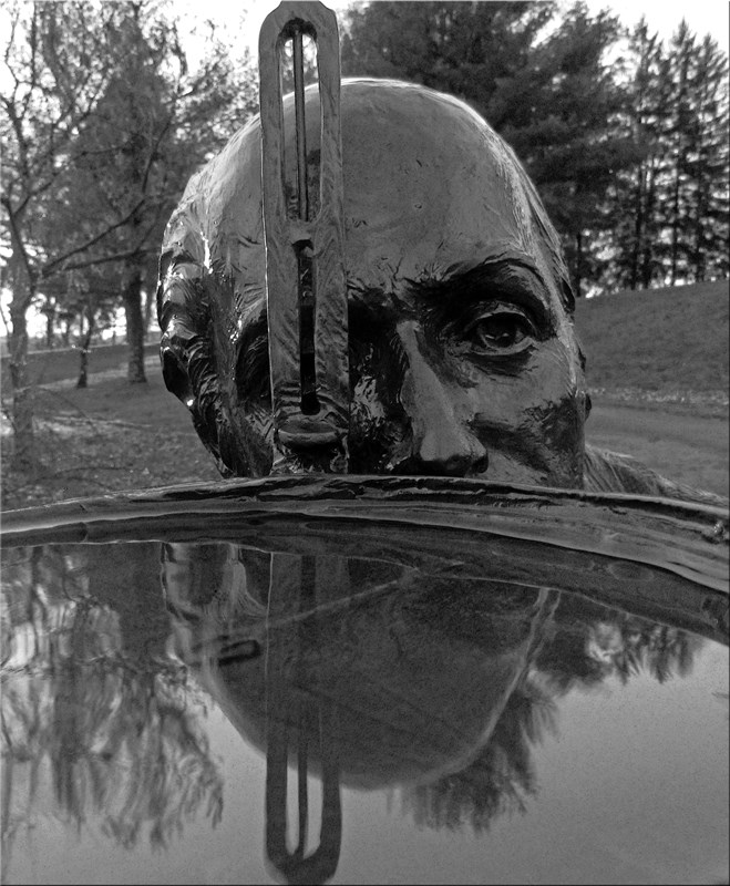 black and white close up of water on surveyor's compass in front of statue of Albert Gallatin