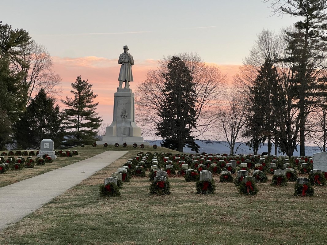 graves with wreaths leaning against the stone. tall soldier monument with pink orange sunset