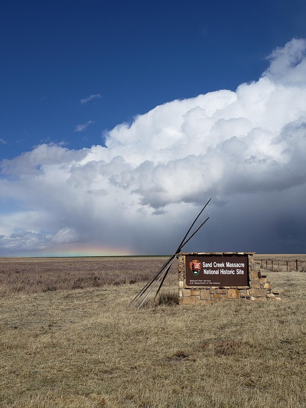The cloud mass of a summer thunderstorm looms in the distance beyond the park entrance sign
