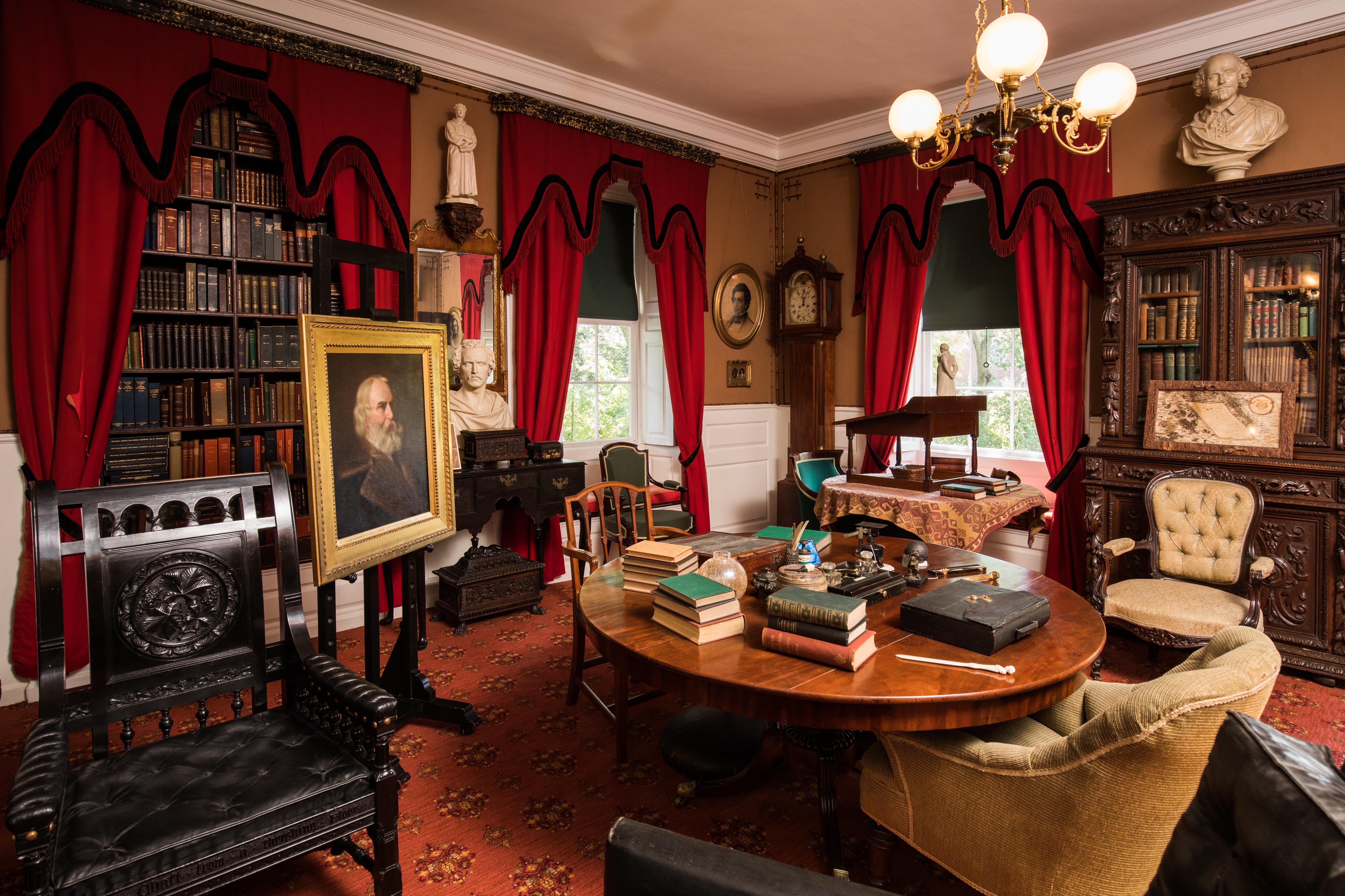 View of a study with a round center table cluttered with books and writing implements.