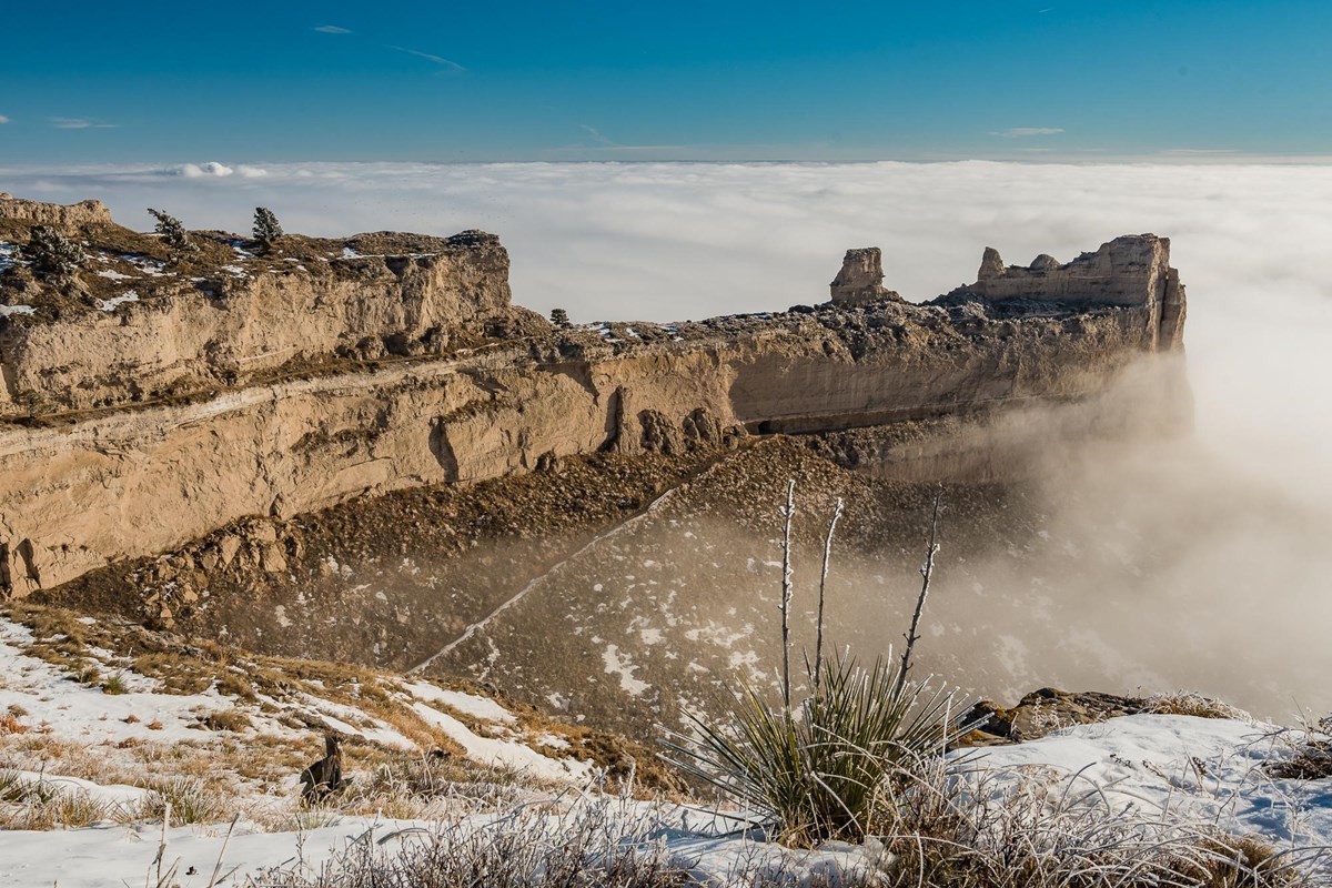 A unique rock formation is seen above a layer of clouds. 