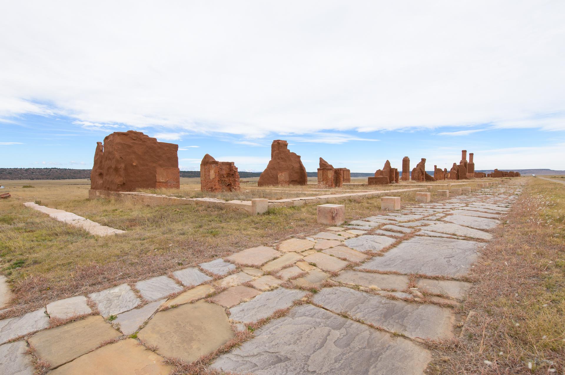 A stone path leads into the distance next to adobe ruins.