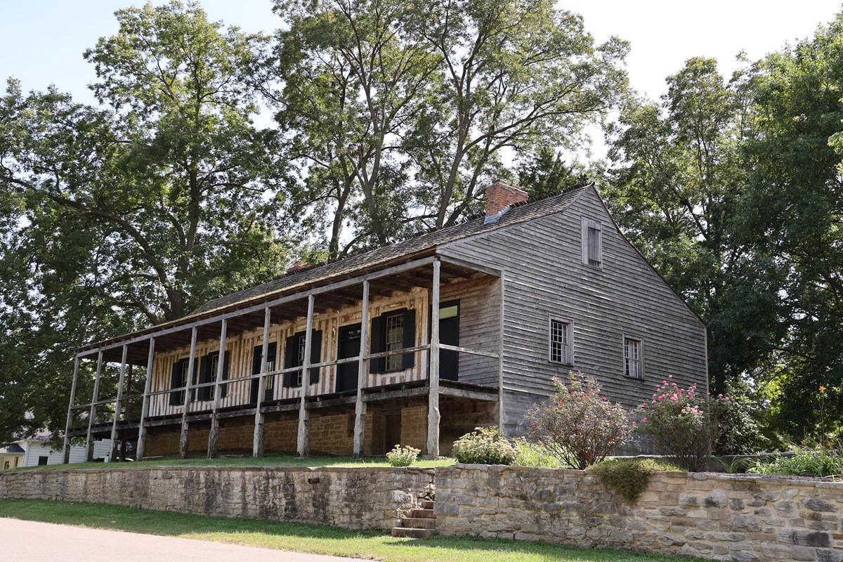 A large raised building with a covered porch and vertical log construction visible. 