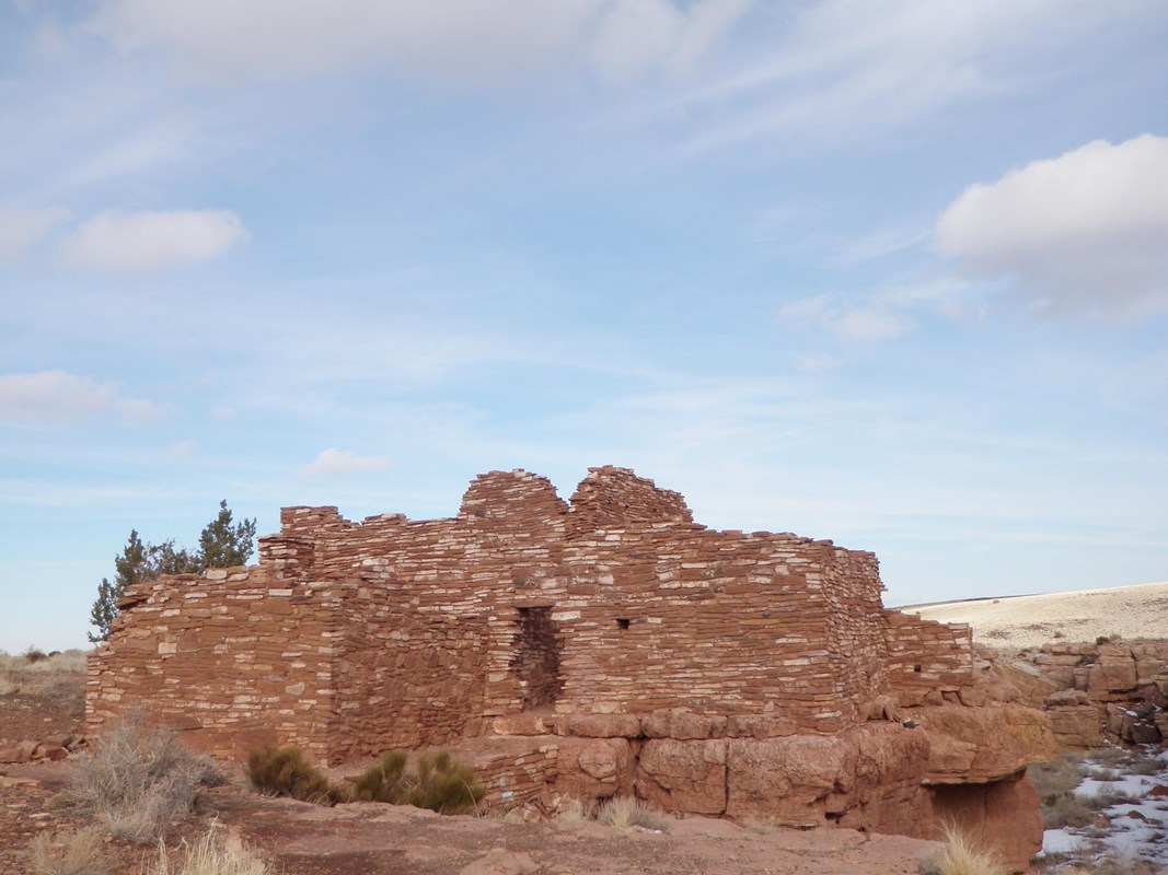 Walls of a white limestone and red sandstone structure under light blue skies with white clouds. 